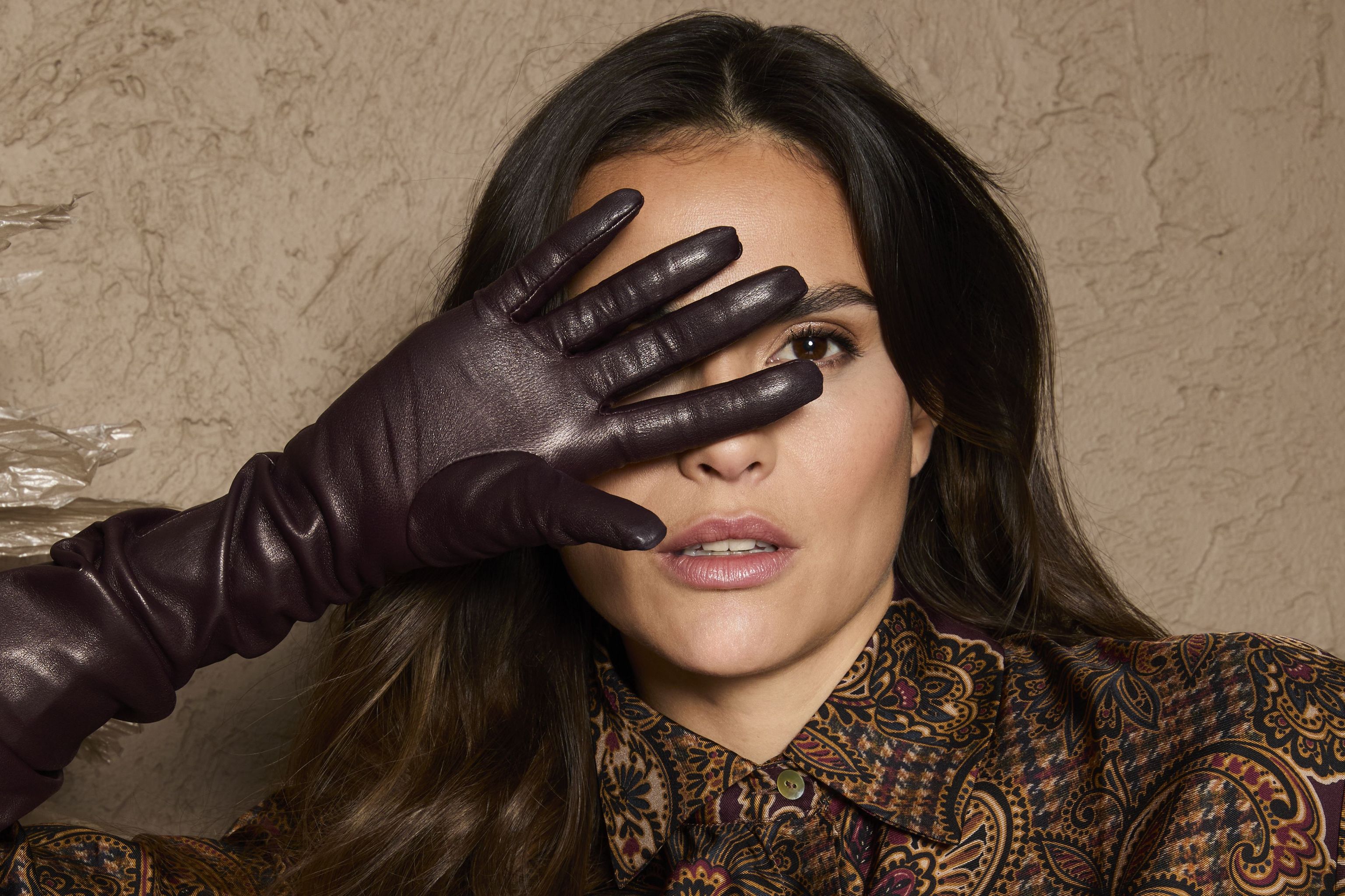 Person mit Hand vor Augen in glamourösem, gemustertem Gewand und Handschuhen.