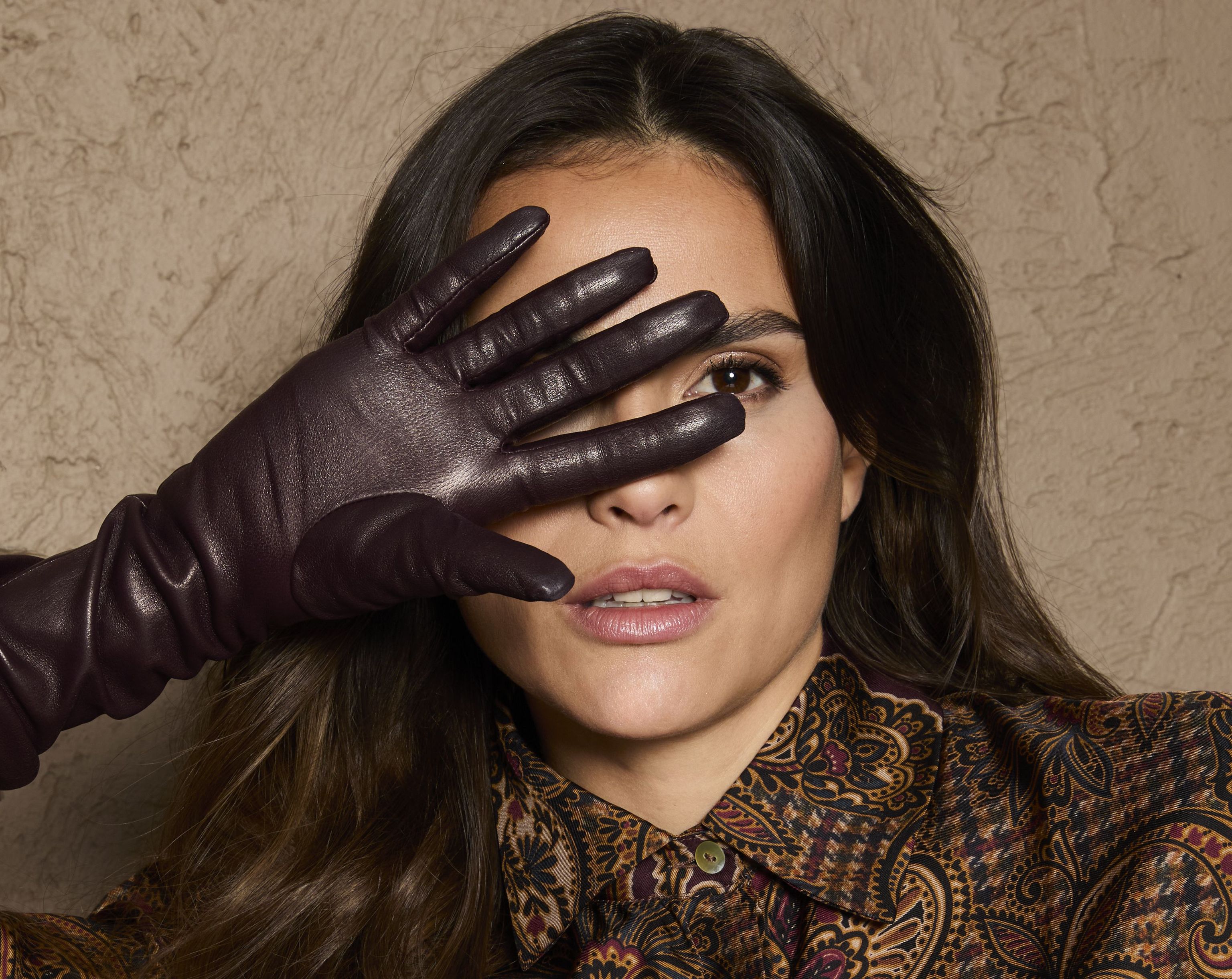 Person mit Hand vor Augen in glamourösem, gemustertem Gewand und Handschuhen.