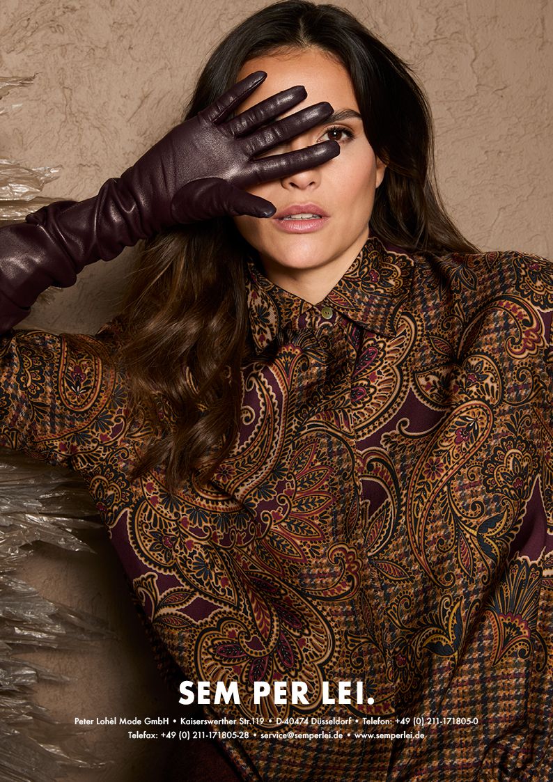 Frau mit elegantem Paisley-Blazer und Handschuhen, mysteriös posierend.