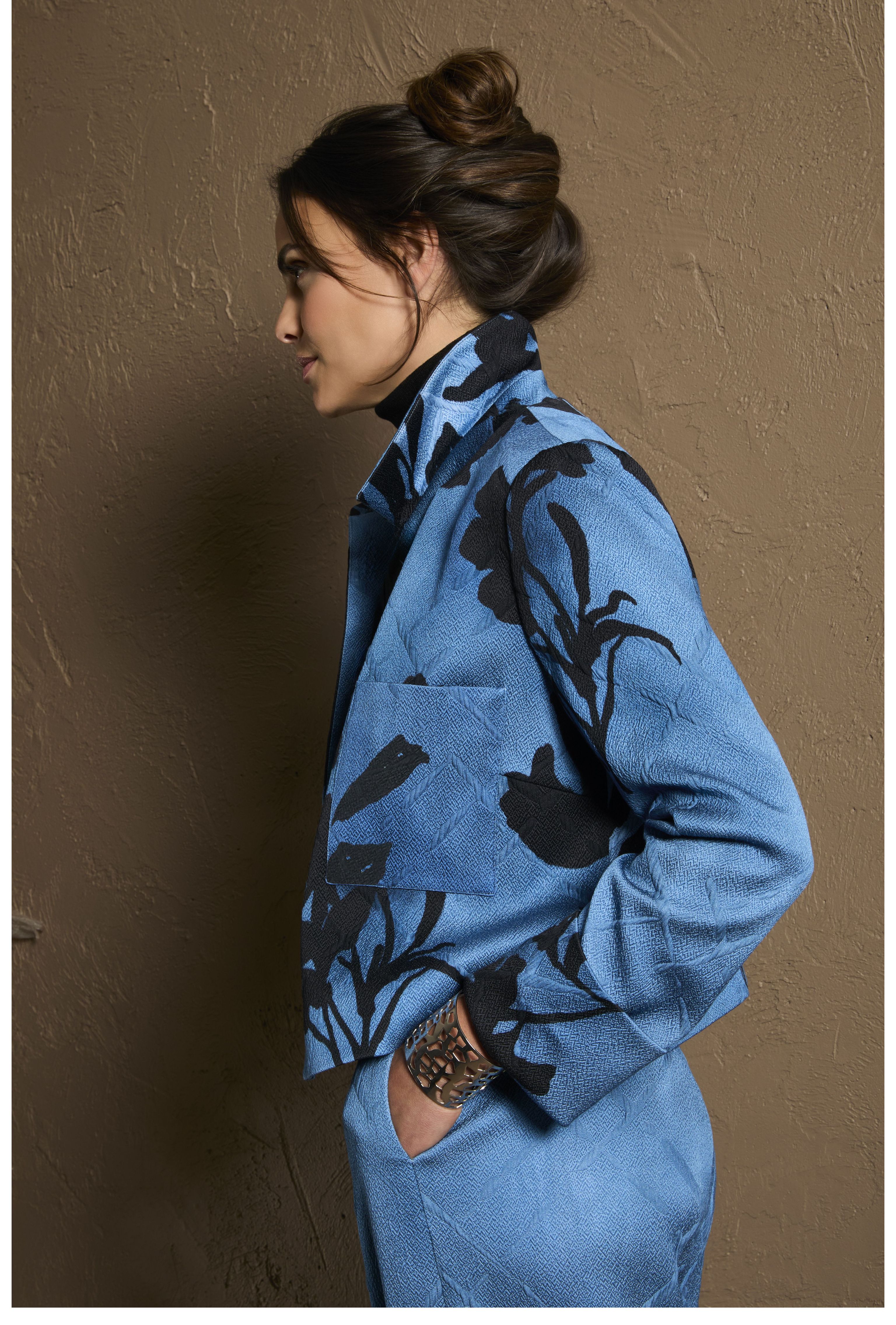 Frau trägt blaues, gemustertes oversized Jacken-Set mit floralen Akzenten, Haar zu Dutt gebunden.