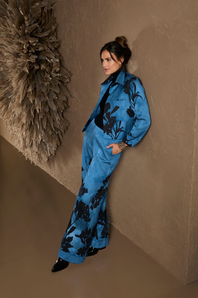 Frau in blauem, floral gemustertem Overall mit schwarzen Akzenten, lässig posierend.